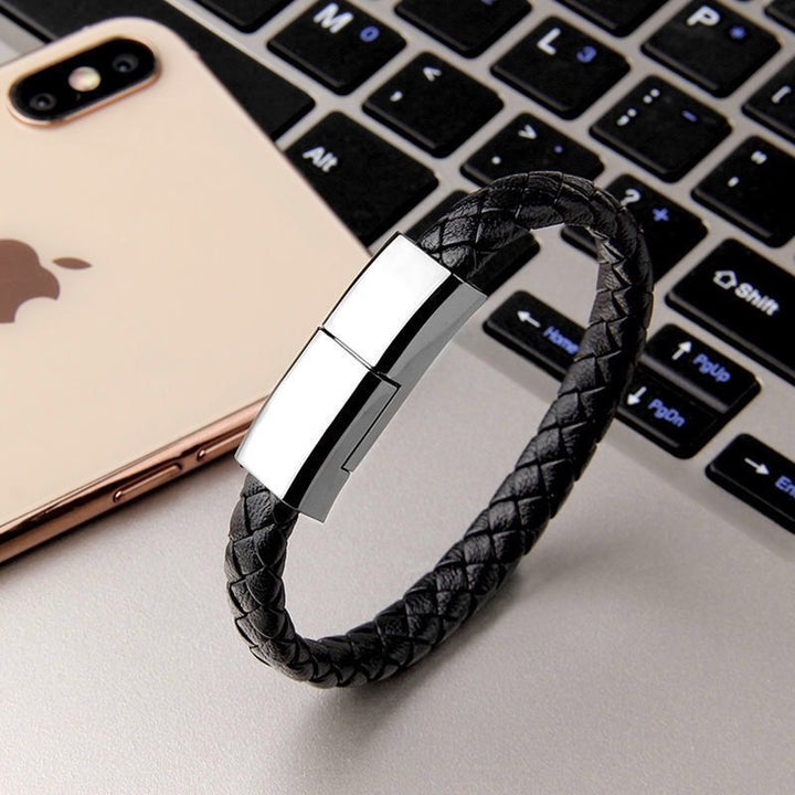 Black braided charging bracelet with silver clasp on laptop keyboard next to smartphone